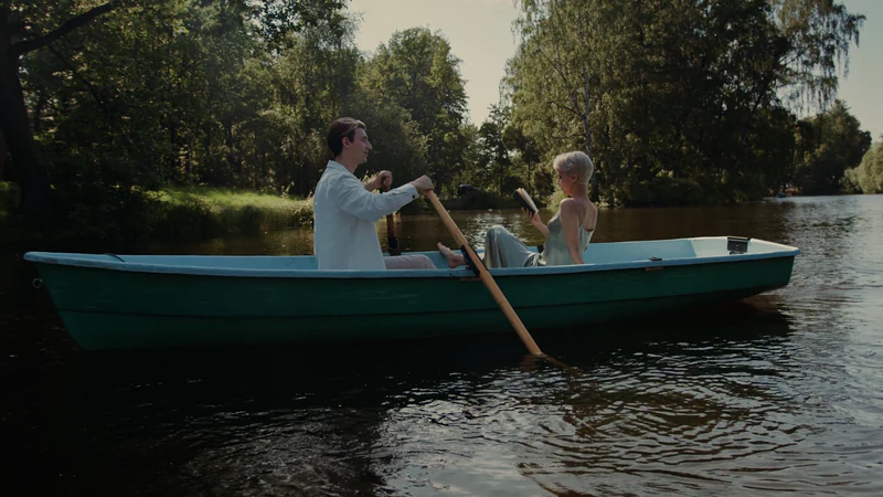 A couple in a rowboat on a lake, trees behind them — after
