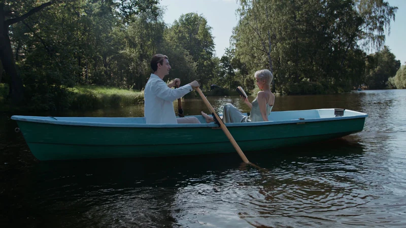 A couple in a rowboat on a lake, trees behind them — before