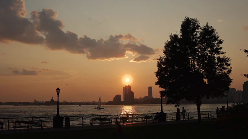 People at a riverside railing as the sun sets behind the skyline — after
