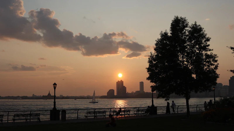 People at a riverside railing as the sun sets behind the skyline — before